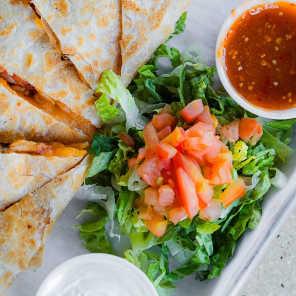 Chicken quesadillas with a side of fresh lettuce, diced tomatoes, salsa, and sour cream.