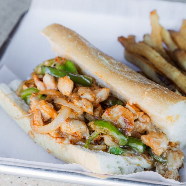 Chicken Philly cheesesteak with green peppers and onions, served with a side of fries.
