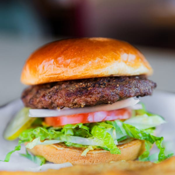 A close-up of a Sammy's Pub and Grill burger with lettuce, tomato, onion, and pickles.