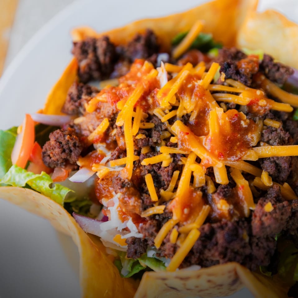 Close-up of a taco salad in a crispy tortilla bowl, topped with seasoned beef, cheese, and salsa.
