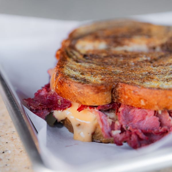 Close-up of a toasted sandwich with pastrami, melted cheese, and sauce on a metal tray.
