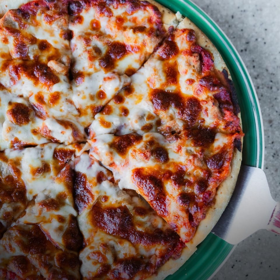 A freshly baked, sliced pizza with melted cheese and tomato sauce on a green plate.